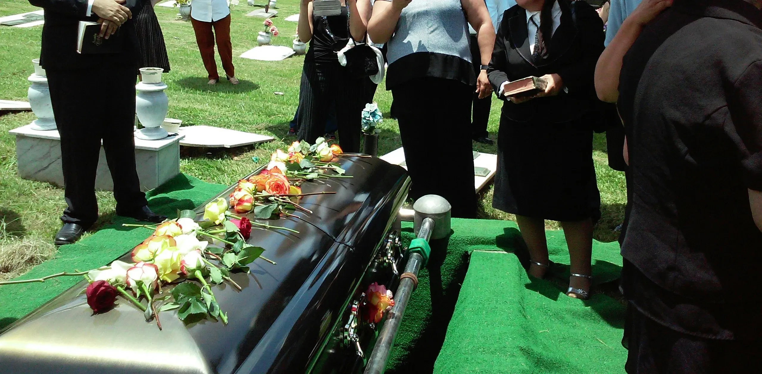 Cérémonie de funérailles au cimetière avec cercueil et roses déposées.