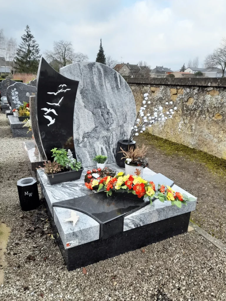 Tombe moderne en granit veiné avec stèle bicolore et gravure d'oiseaux.