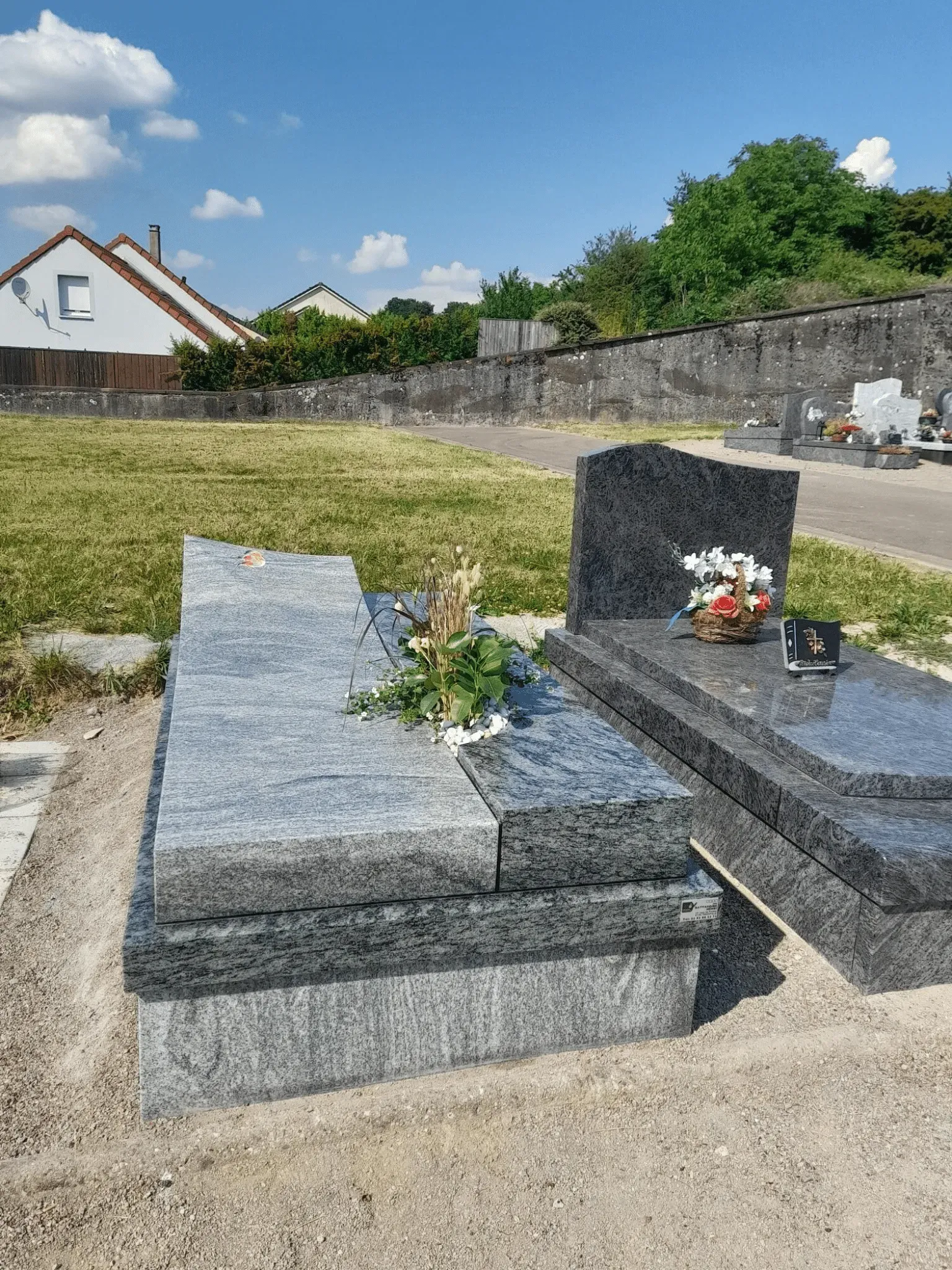 Monument funéraire simple en granit gris veiné avec pierre tombale moderne et fleurs.