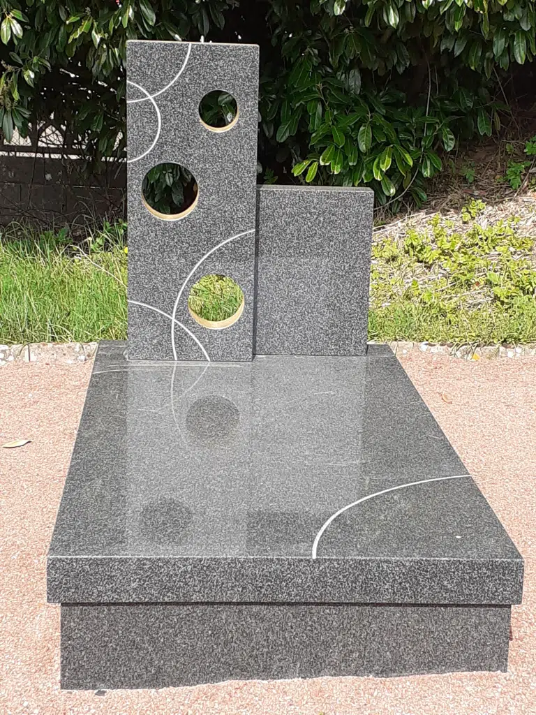 Petit monument funéraire moderne en granit poli avec découpes géométriques.