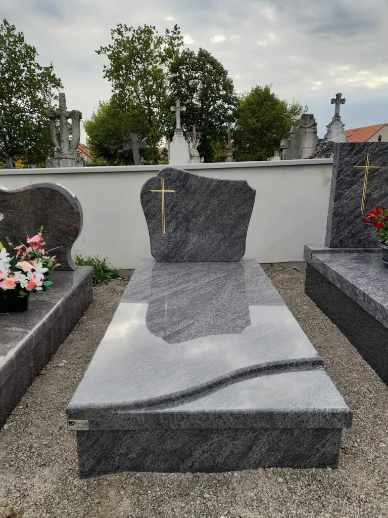 Monument funéraire en granit bleu poli avec stèle galbée et croix dorée.