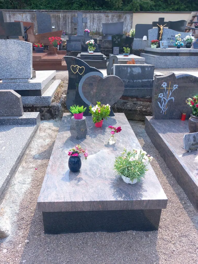 Monument funéraire double en granit rose avec stèle gravée et motifs cœurs.