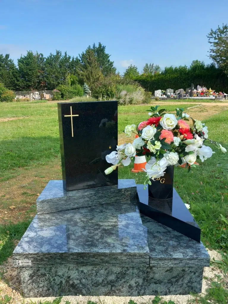 Petit monument funéraire moderne avec croix dorée et composition florale.