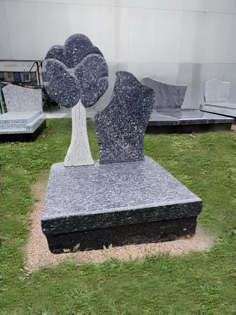 Monument cinéraire moderne en granit gris avec stèle sculptée en forme d'arbre.