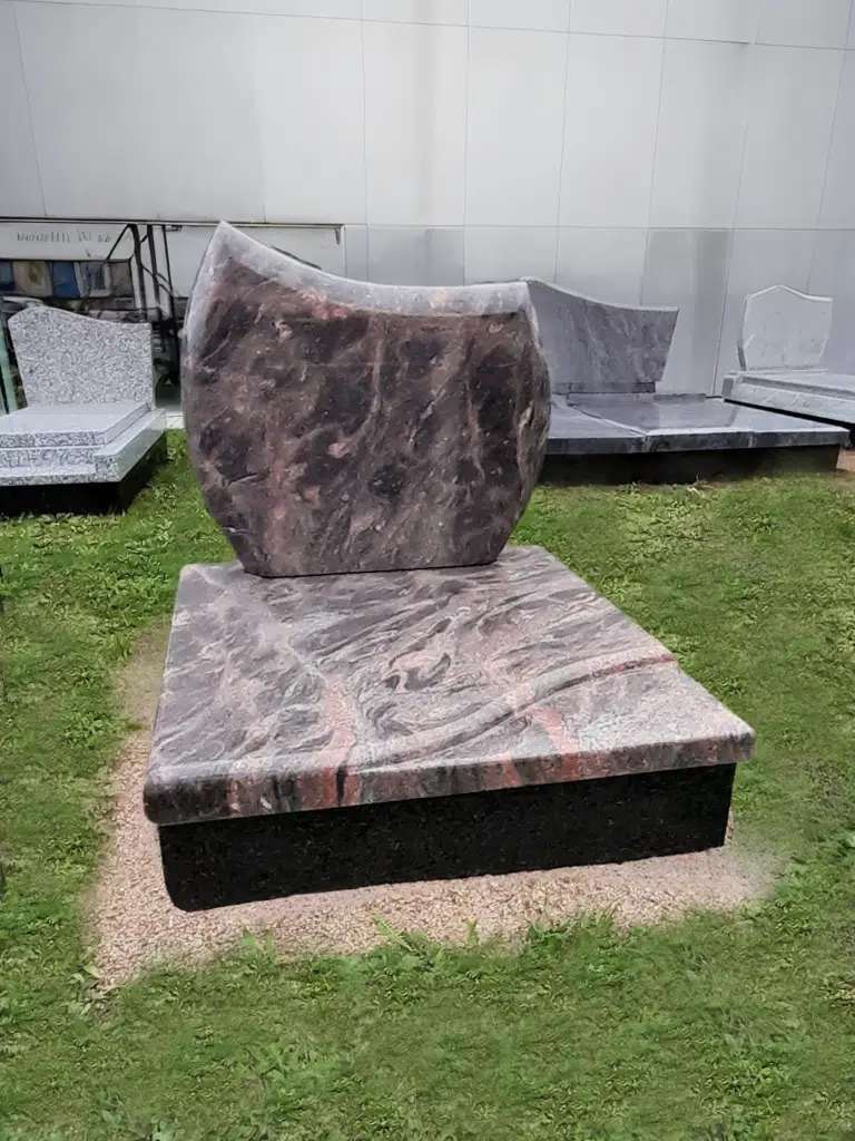 Petit monument cinéraire en granit veiné rose et noir avec stèle aux formes arrondies.