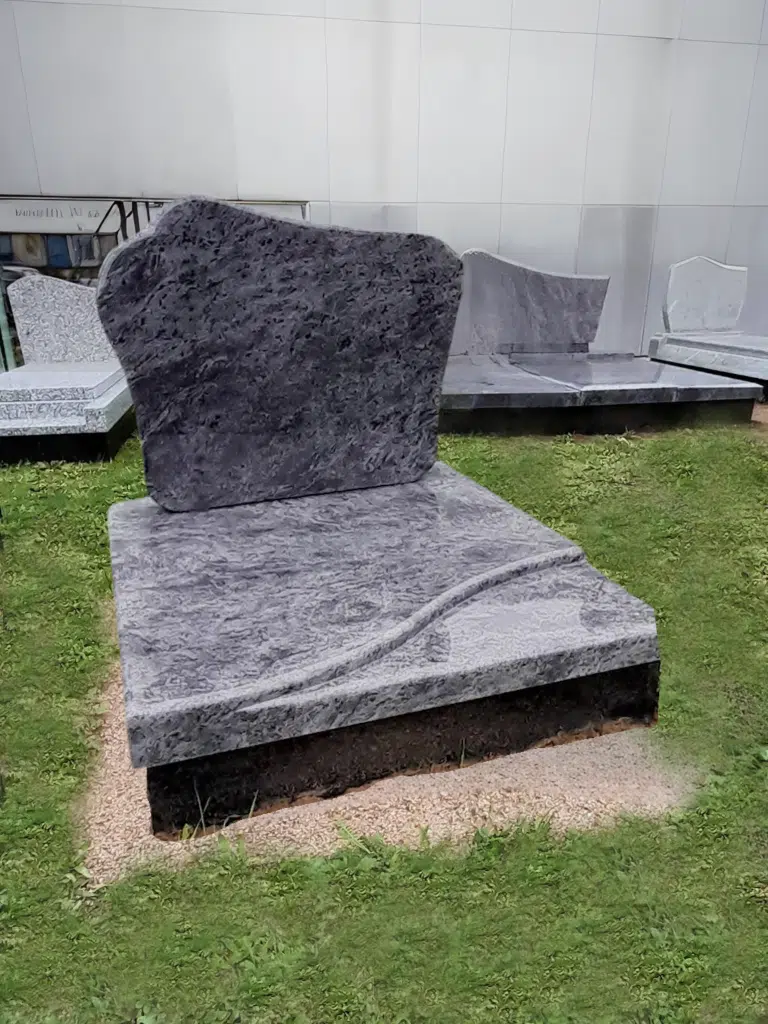 Monument funéraire cinéraire en granit bleu veiné avec motif de vague sculpté.